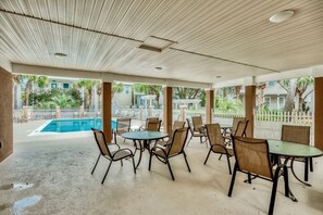 Ein Terrassenbereich im Freien mit Tischen und Stühlen, ein Pool im Hintergrund und Blick auf Häuser und Grünflächen.