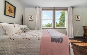 A bedroom with a large bed, a window with a view of greenery, and two framed pictures on the wall. - The Gingerbread Nest, a private nature retreat (Glasgow)