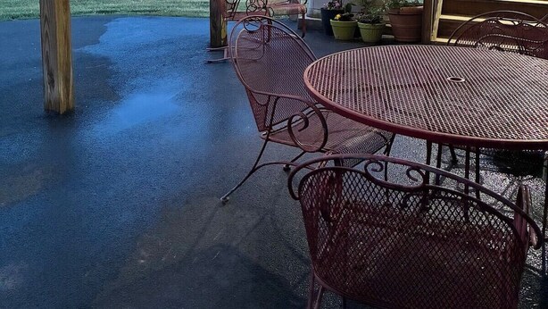 Eine Terrasse im Freien mit Metallstühlen und einem Tisch, ein Holzboden und Blick auf einen bewaldeten Bereich.