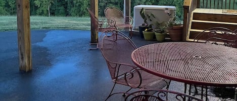 Un patio exterior con sillas y una mesa de metal, una terraza de madera y vistas a un área boscosa.