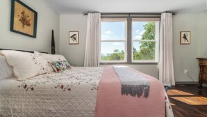 Ein Schlafzimmer mit einem großen Bett, zwei Fenstern mit Vorhängen und Blick auf Grünfläche.