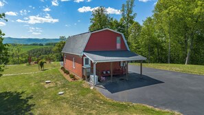 A red barn with a covered porch and a paved driveway.