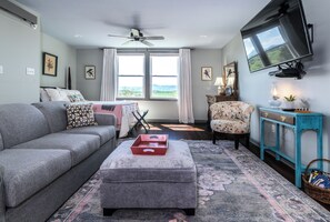 A living room with a sofa, ottoman, and a television mounted on the wall.