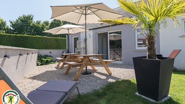 Een terras met een tafel, stoelen, een grote parasol en een plant in pot.