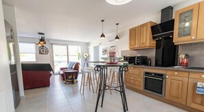 A modern kitchen with wooden cabinets, a black refrigerator, and a dining area with stools.