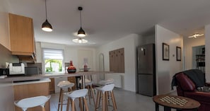 A modern kitchen with a central island, bar stools, a refrigerator, and a chess table.