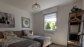 Een slaapkamer met twee bedden, een radiator, een raam met zonwering, een hanglamp en een houten garderobe.