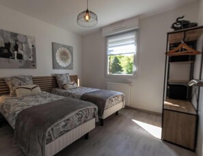 A bedroom with two beds, a radiator, a window with blinds, a hanging light fixture, and a wooden wardrobe.