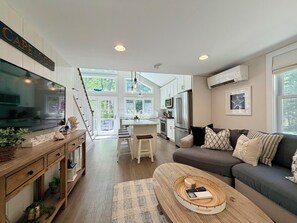 Eine moderne Küche mit einer zentralen Kochinsel, ein Essbereich mit einer Bank, ein Wohnzimmer mit einer Couch und große Fenster.