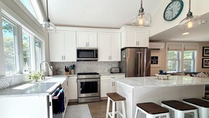 Una cocina moderna con gabinetes blancos, electrodomésticos de acero inoxidable y una isla grande con taburetes de bar.