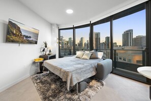 Ein modernes Schlafzimmer mit Blick auf die Stadt, einem großen Bett, einem Nachttisch und einem Stadtbildgemälde.