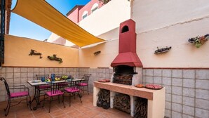 Un patio al aire libre con piso de ladrillo, una mesa con sillas, una parrilla y un toldo amarillo.