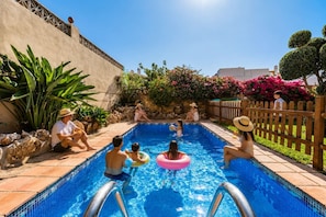 Ein Schwimmbecken mit Personen in der Nähe, umgeben von Pflanzen und einem Holzzaun.