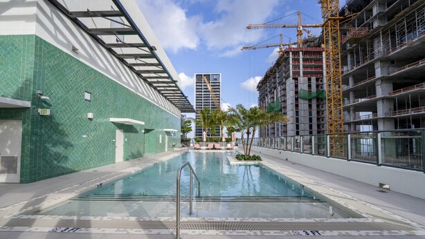 A swimming pool with a metal ladder, a green tiled wall, and a construction crane in the background.
