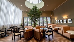 A modern lounge area with round tables, cushioned seating, a large tree, and a skylight.