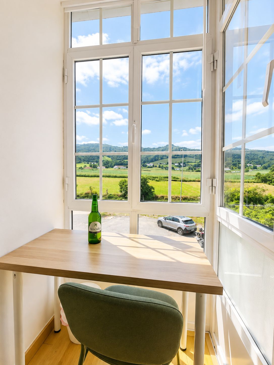 Una habitación con un ventanal grande, una mesa de madera y una silla verde.