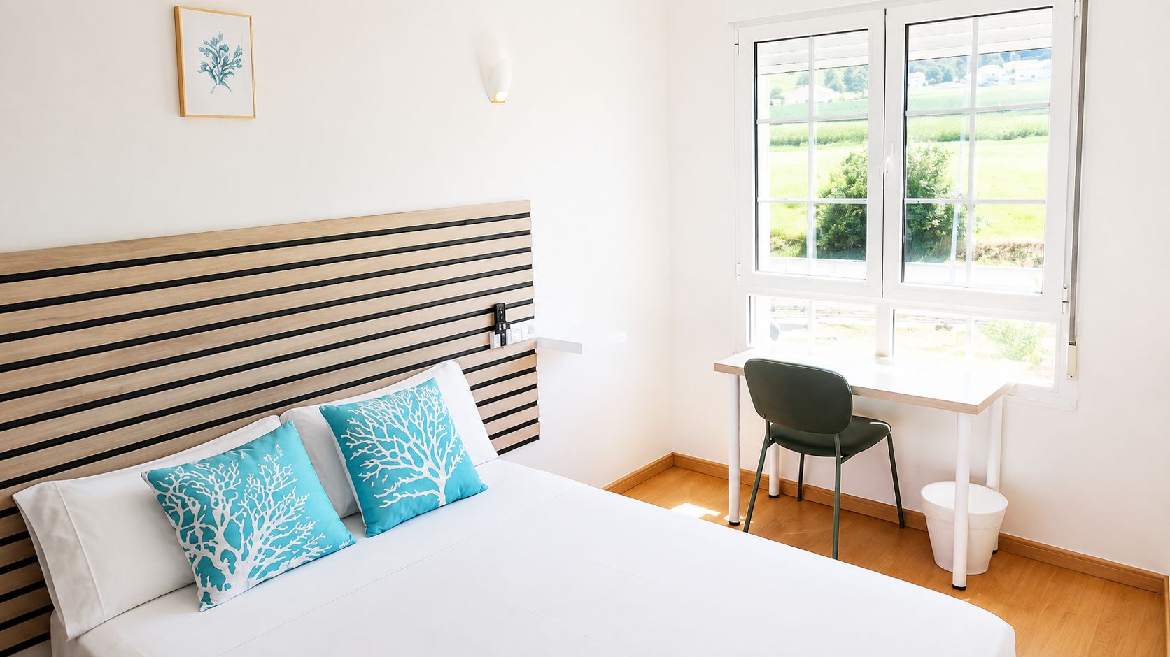 Un dormitorio con cama, escritorio y silla. Hay una ventana con vistas a zonas verdes.