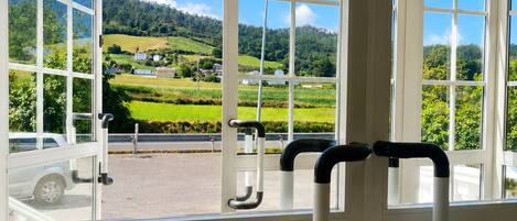Una habitación con ventanas amplias que ofrecen vistas a un paisaje verde y un coche aparcado afuera.