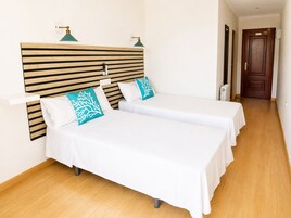 Habitación de hotel con dos camas, cabecera de madera y pared blanca.