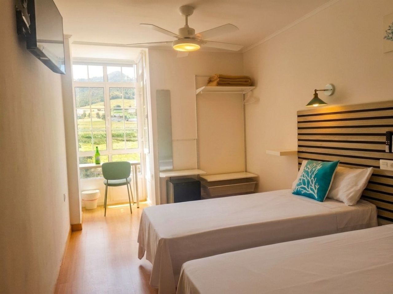 Ein Hotelzimmer mit zwei Betten, einem Schreibtisch, einem Stuhl und einem Fenster mit Blick auf Grünflächen.
