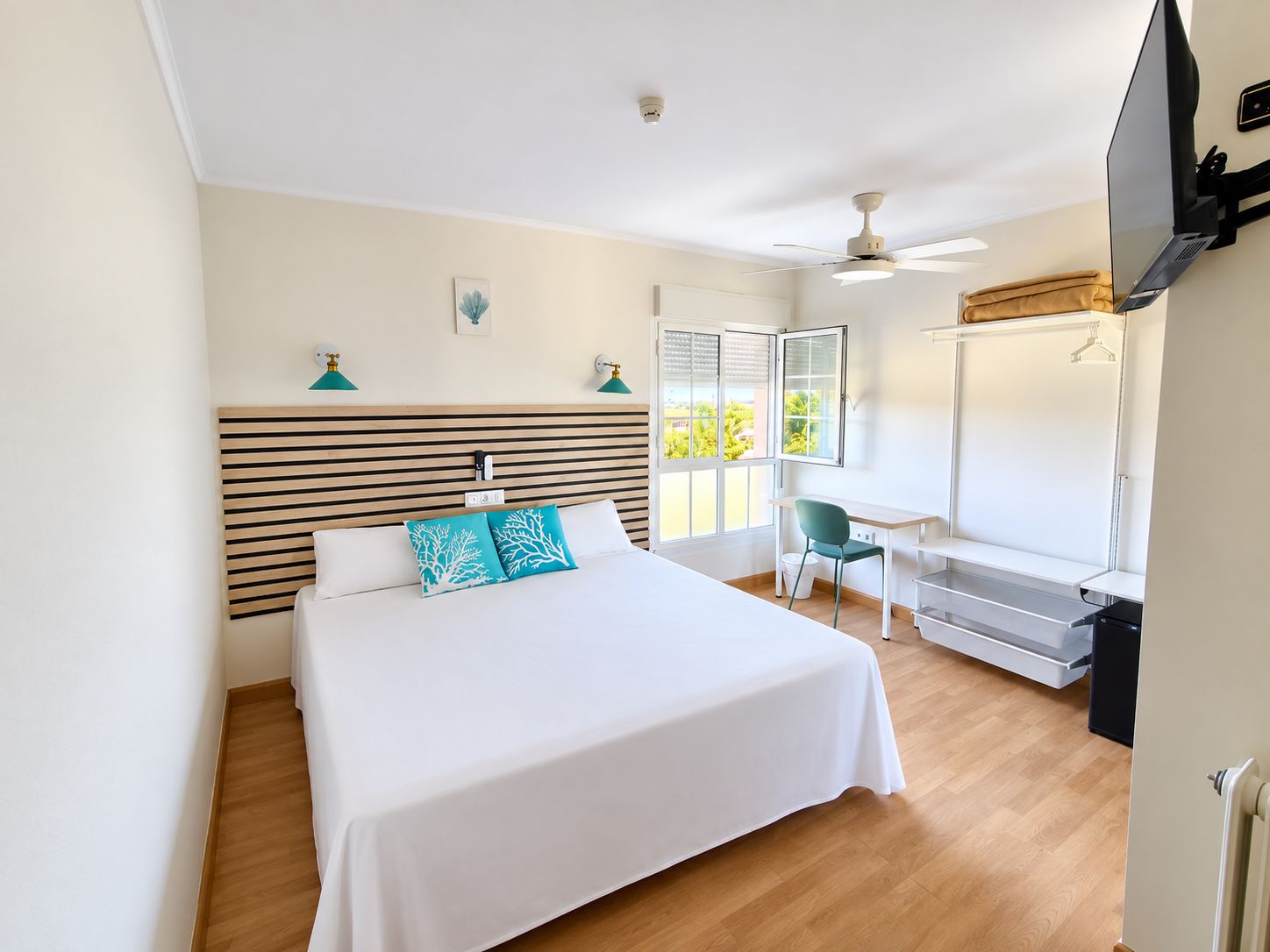 A hotel room with a bed, desk, chair, and a window with blinds.