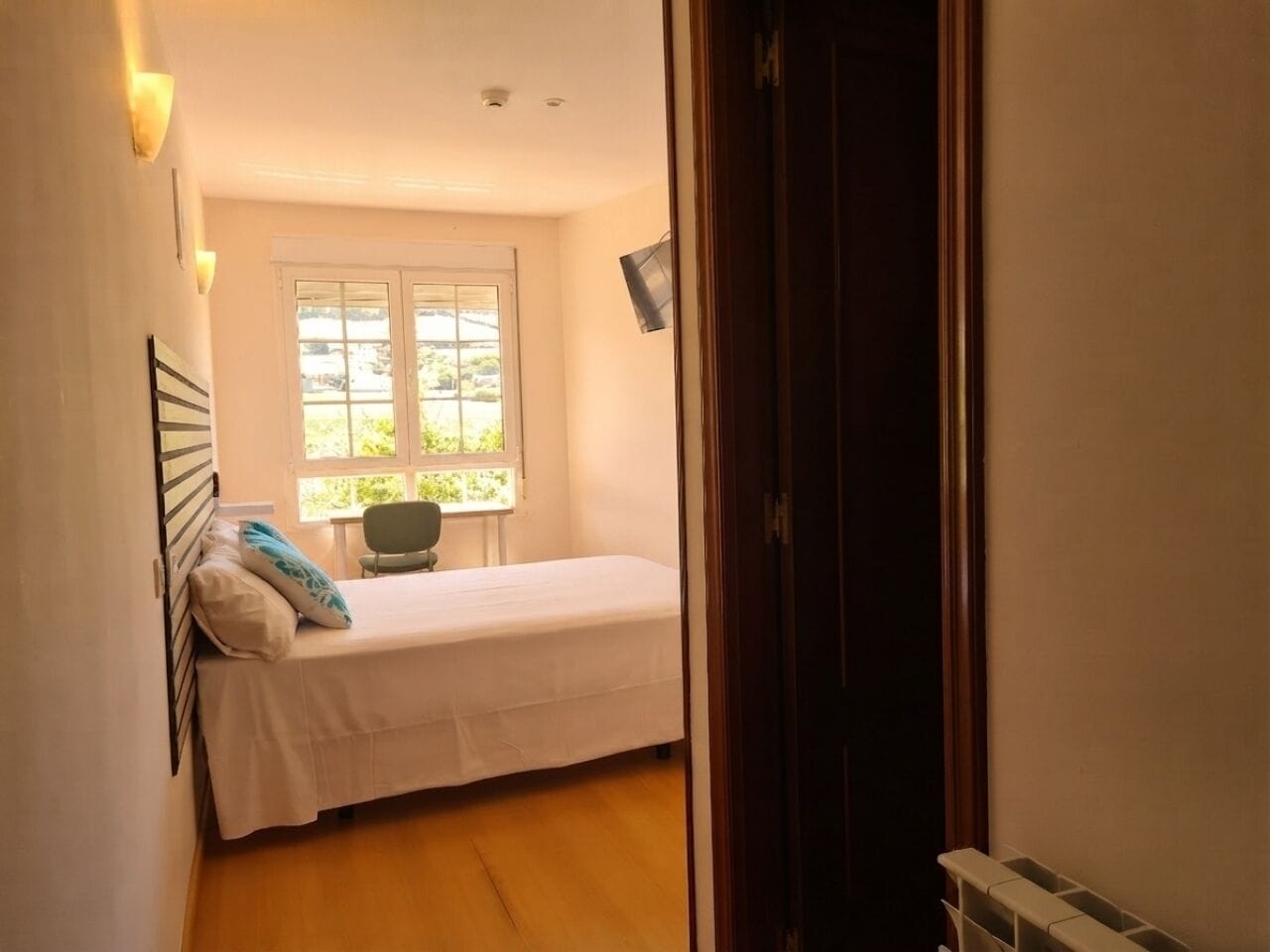 Un dormitorio pequeño con una cama individual, una silla, un ventanal y un radiador.