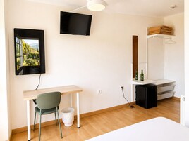 Una habitación minimalista con escritorio, silla, televisor y vistas a un paisaje por la ventana.