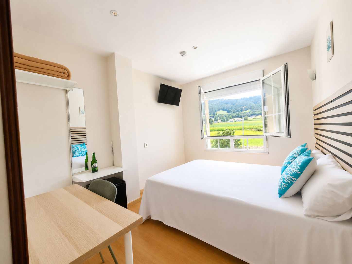 Un dormitorio con cama, escritorio, silla, televisor y ventana con vistas al paisaje.