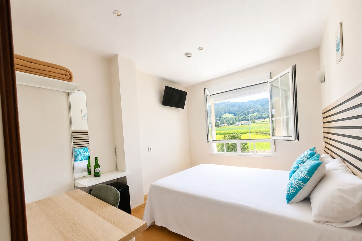 Un dormitorio con cama, escritorio, silla, televisor y ventana con vistas al paisaje.