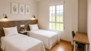 A bedroom with two beds, a ceiling fan, a window with a view, and a small table. - Hotel Peña Pintada (Valdes)