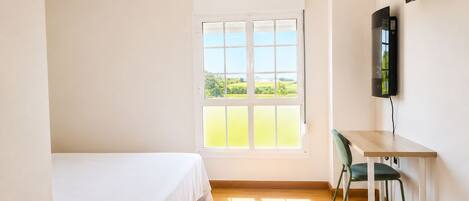 Une chambre avec un lit, un bureau, une chaise, une télévision et une fenêtre donnant sur un paysage verdoyant.
