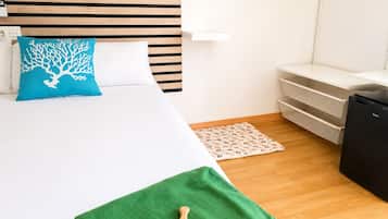 A hotel room with a bed, a nightstand, a desk, a chair, and a small kitchenette.
