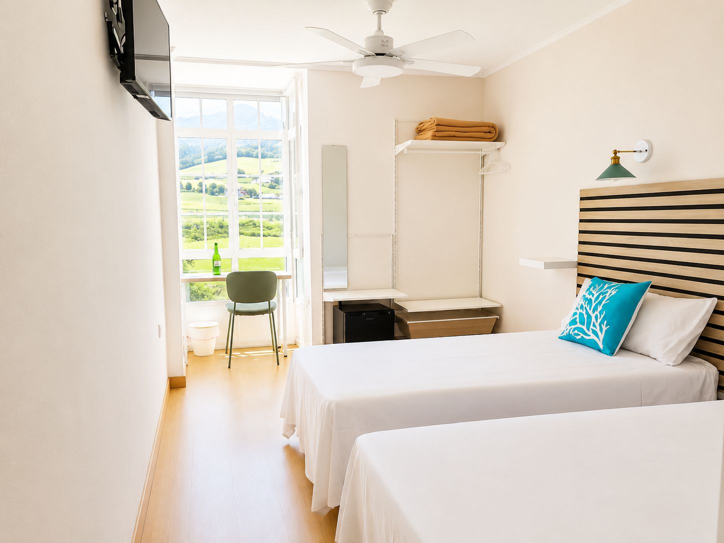 Een hotelkamer met twee bedden, een bureau, een stoel, een televisie, een plafondventilator en een raam met uitzicht op het landschap.