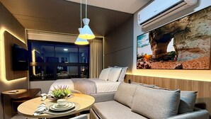 Ett modernt vardagsrum med en soffa, ett matbord med stolar, en tv som är monterad på väggen och en luftkonditioneringsanläggning.