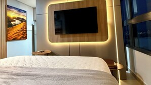 Ett modernt hotellrum med en stor s äng, en väggmonterad TV och en tavla som föreställer ett ökenlandskap.