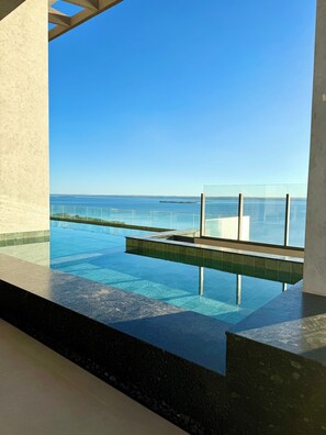 Vista chiara di una piscina a sfioro con barriera in vetro, che si apre su un ampio specchio d'acqua.