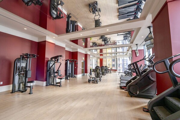 Ett rymligt gym med konditionsmaskiner, styrketräningsstationer och en fin utsikt över staden genom stora fönster.
