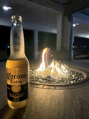 A bottle of Corona Extra beer and a fire pit with burning logs.