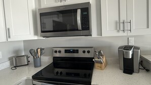 A kitchen with white cabinets, a stainless steel microwave, a black oven, a toaster, and a coffee maker. - Relaxing Coastal Retreat in Cape May! Condo #8 (Cape May)