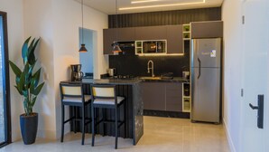 Een moderne keuken met een centraal eiland, barstoelen, een koelkast en een potplant.