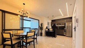 Een moderne keuken met een roestvrijstalen koelkast, een eethoek met een ronde tafel en stoelen, en een groot raam dat zorgt voor natuurlijk licht.