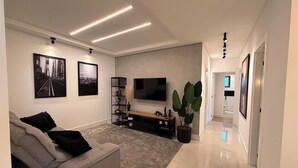 Een moderne woonkamer met een grijze bank, een flatscreen televisie en een grote potplant.