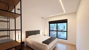 Een moderne slaapkamer met een bed, een inbouwplank, een raam met uitzicht op de stad en een houten vloer.