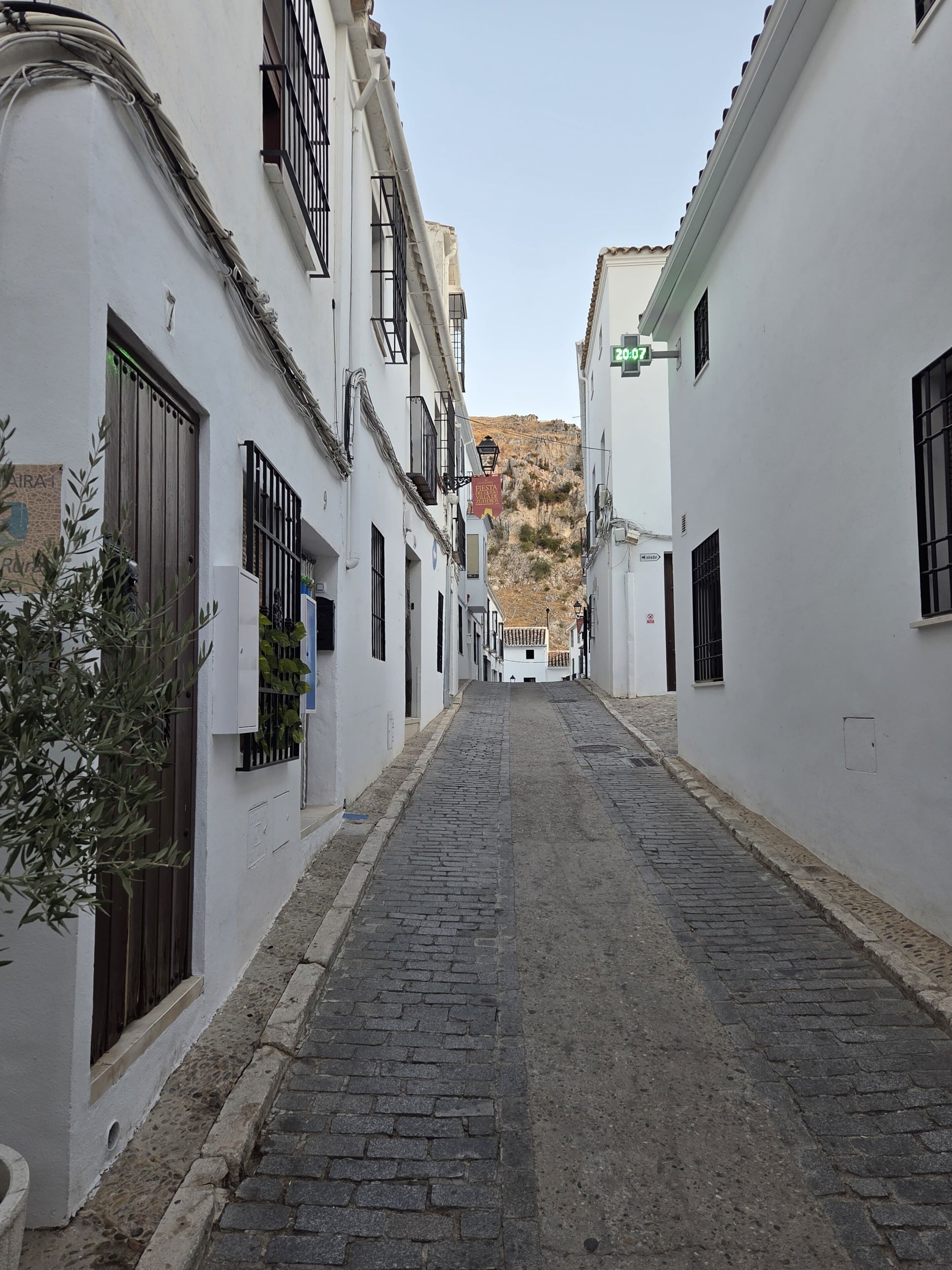 Una estrecha calle empedrada bordeada de edificios blancos con rejas y balcones.