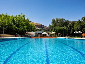 A clear blue swimming pool with diving lanes, surrounded by trees and a building with a white facade.