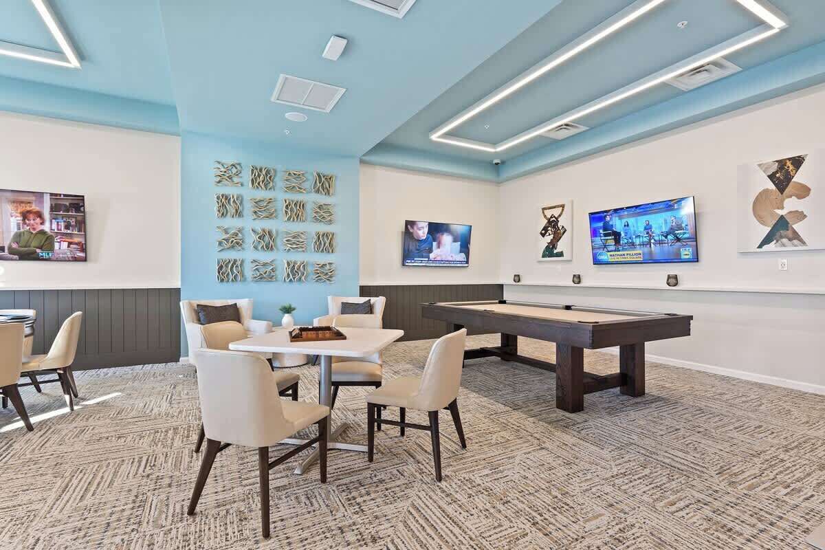 A modern lounge area with a pool table, comfortable seating, and wall-mounted televisions.