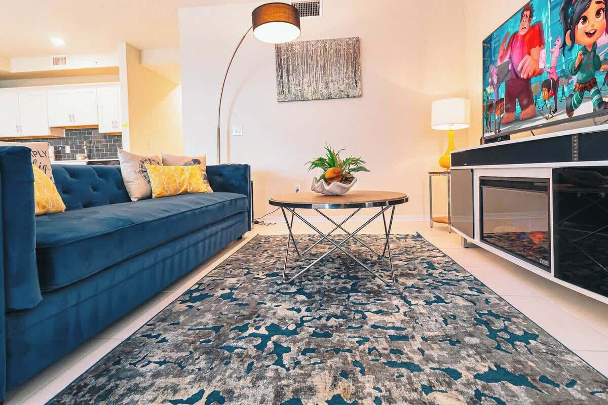 Een woonkamer met een blauwe bank, een ronde salontafel, een televisie en een open haard.