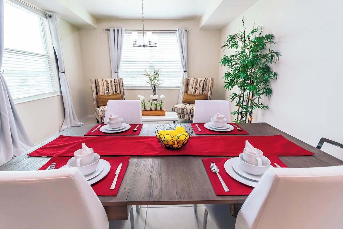 A dining area with a wooden table, red placemats, white plates, and a central yellow fruit bowl.