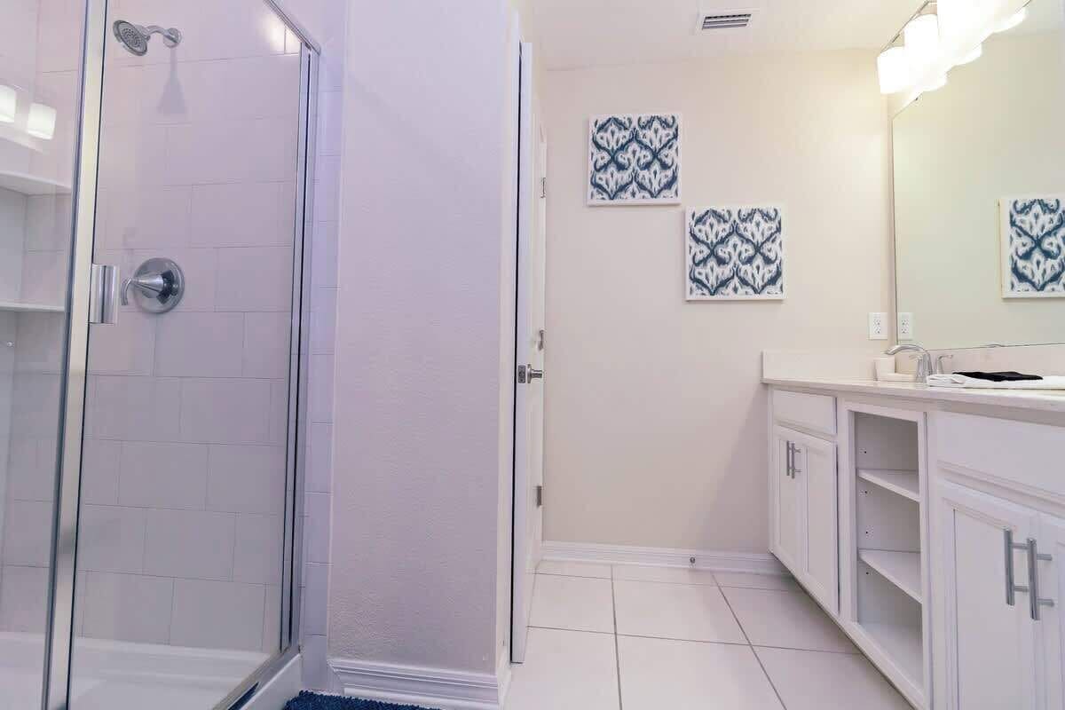 A bathroom with a glass shower enclosure, white tiled walls, and a vanity with a mirror.