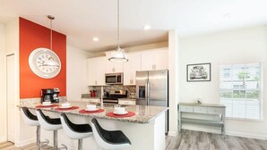 A modern kitchen with a central island, bar stools, a clock, and a dining area with a bench. - Cozy Home in Amazing Resort for Perfect Vacations (Davenport)